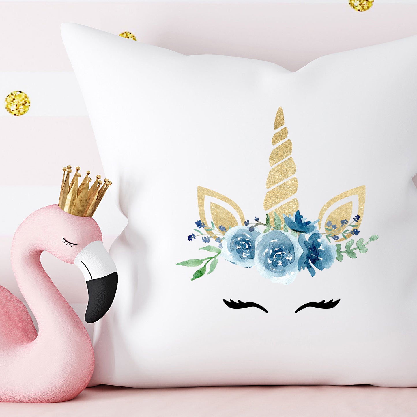 Flamingo plush toy with a crown next to a decorative pillow with unicorn design on a pink background