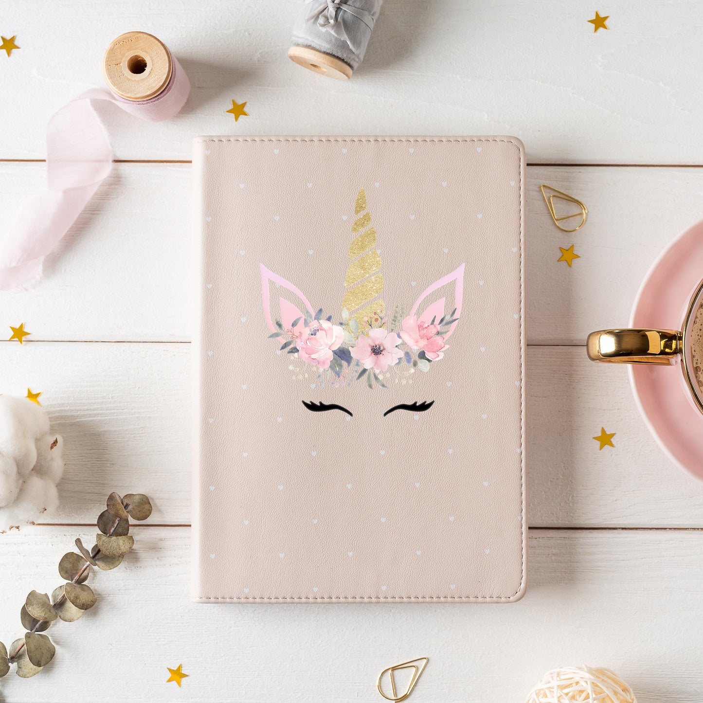 Unicorn-themed notebook with floral design on a light wooden surface with decorative items.