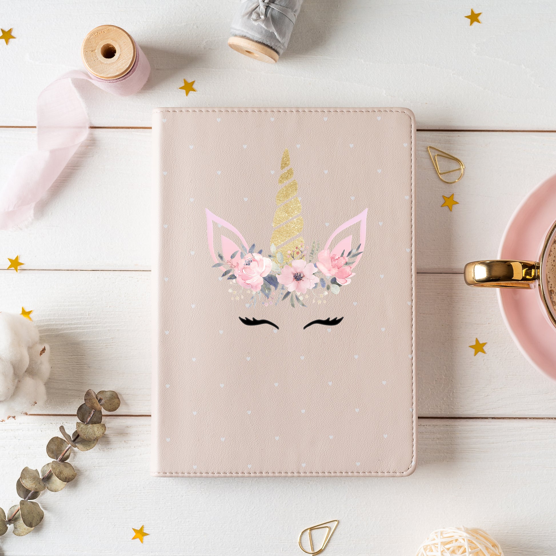 Unicorn-themed notebook with floral design on a light wooden surface with decorative items.