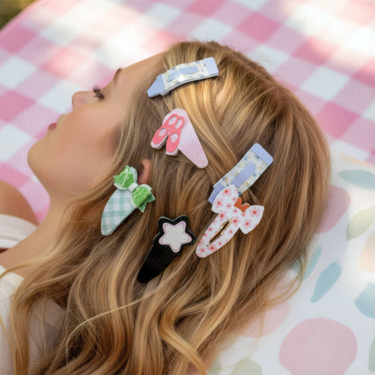 A close-up lifestyle shot of a woman lying down with her hair, wearing six cute, pastel-colored fabric hair clips with various patterns like gingham, polka dots, and stars.
