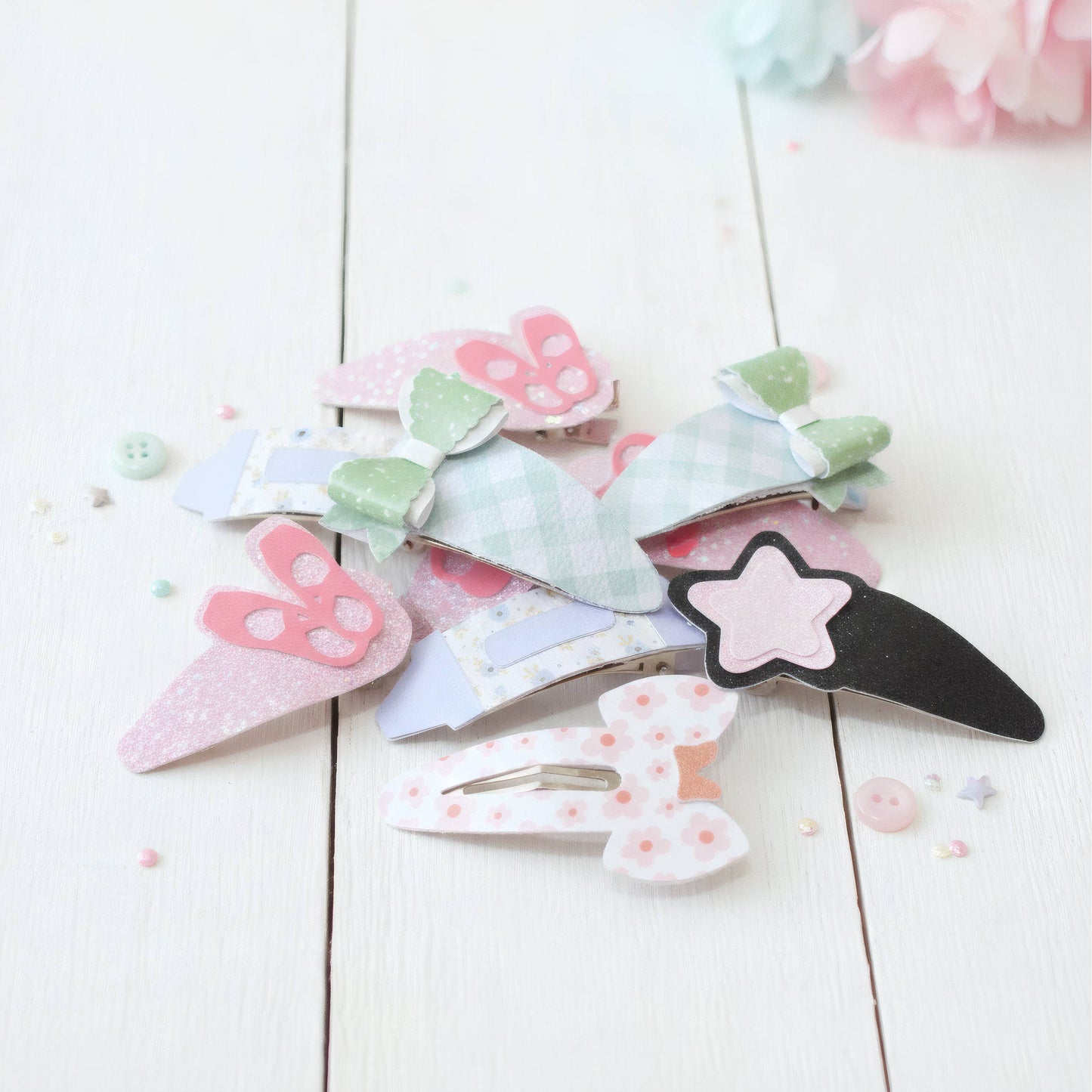 A pile of pastel paper clip hair accessories on a white wooden surface, including bunny, bow, and star designs in pink, green, blue, and black.
