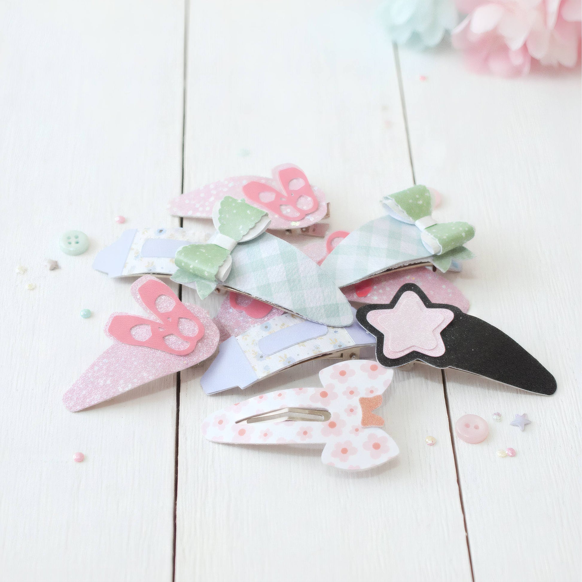 A pile of pastel paper clip hair accessories on a white wooden surface, including bunny, bow, and star designs in pink, green, blue, and black.