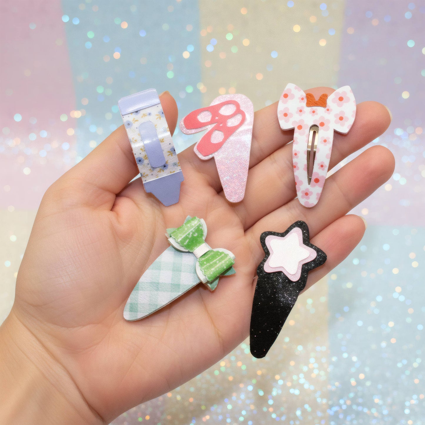 A hand holds five cute, pastel-themed hair claw clips against a sparkly pastel background. The clips feature designs including a lavender flower, a pink mushroom, a white bow with pink dots, a green-and-white checkered leaf, and a black star-shaped clip.