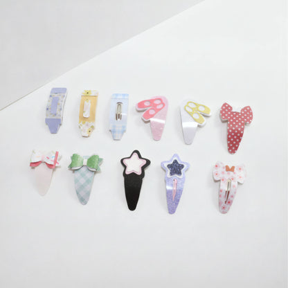 A set of ten cute, pastel-colored hair clips arranged in two rows on a clean white background. The clips feature various designs including bows, stars, and ice cream cones in different patterns like polka dots, stripes, and glitter.