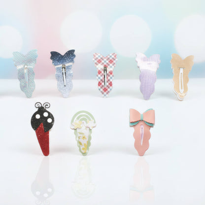 Eight decorative hair claw clips arranged on a white surface with a soft pastel bokeh background. The clips feature various designs including butterflies, ice cream cones, a ladybug, and bows in pastel and patterned colors.
