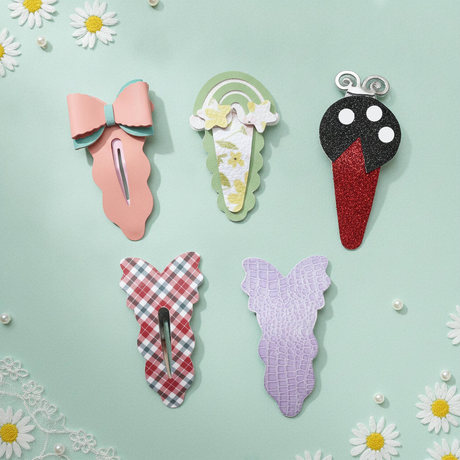 Five decorative hair claw clips arranged on a mint green background with white daisy flowers and lace trim. The clips include a pink bow, a green rainbow, a black-and-red ice cream cone, a red-and-white gingham butterfly, and a lavender crocodile-texture butterfly.