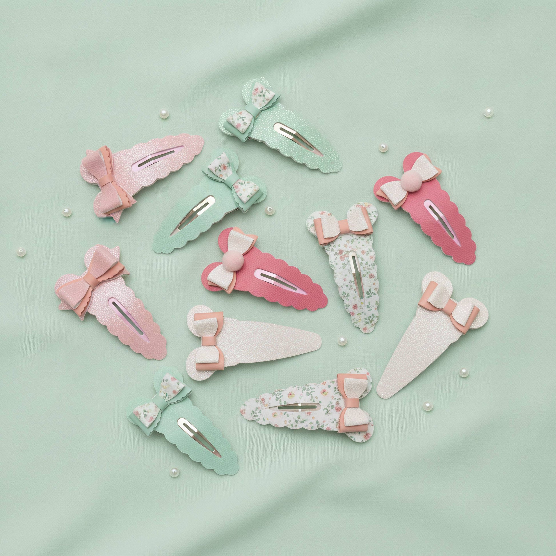 A set of pastel hair claw clips arranged on a mint green fabric background with small pearl-like beads. The clips come in pink, mint green, white, and floral print, each decorated with a small bow and ribbon accent.