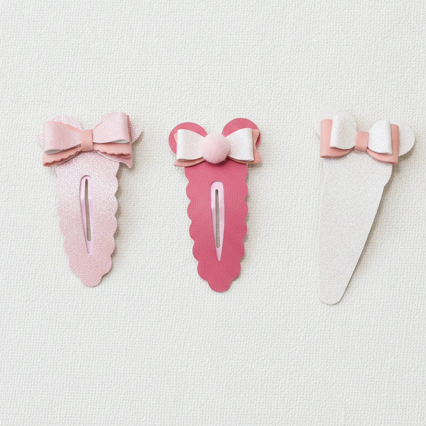 Three pink hair clips with bow details, arranged horizontally on a textured white background.