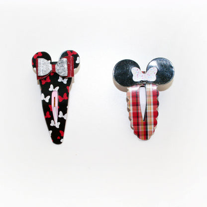 Two Mouse-themed hair clips on a white background. One clip features a black base with red and white patterns, and the other features a red and green plaid pattern with a black top and a white bow detail.