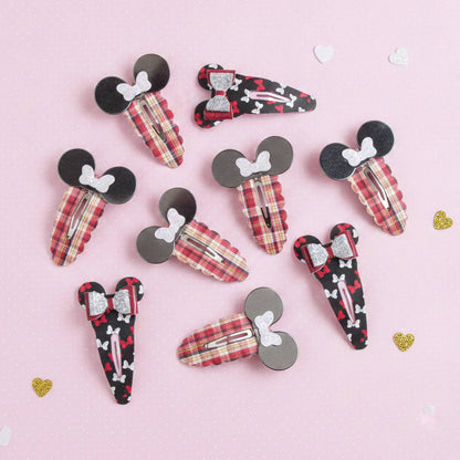 A set of ten hair claw clips styled like Mouse and Minnie Mouse silhouettes, arranged on a light pink background with small scattered heart decorations. The clips feature various fabric patterns including red and beige plaid, black and red hearts, and black and white stripes, with some clips featuring glittery silver bows.