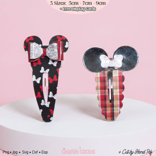 Two Mouse-themed hair clips displayed on a white round pedestal against a pink background. One clip has a black base with red and white bow and butterfly patterns, and a silver glitter bow.
