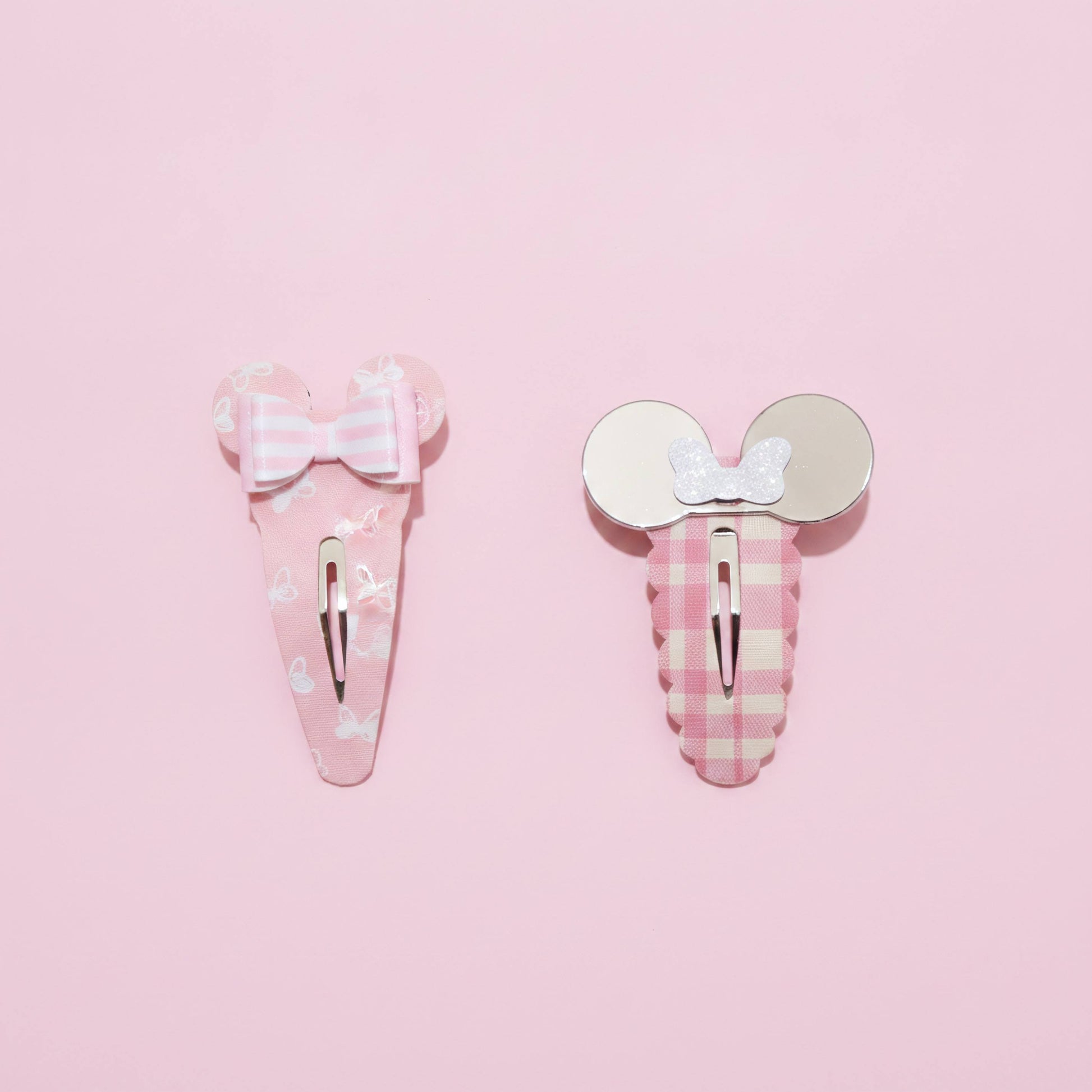Two pink hair clips on a solid pink background. One clip features a Mouse inspired bow on a pink and white striped background with small white bunny prints.