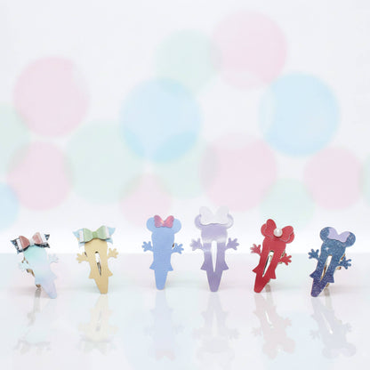 Six colorful, die-cut mouse -shaped  hair clips are lined up on a reflective white surface against a soft, pastel bokeh background of pink, blue, and green circles.