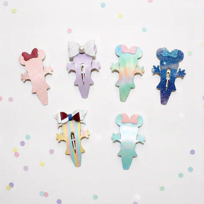 Six colorful mouse-shaped hair clips arranged on a white background with scattered pastel confetti. The clips feature different pastel designs including pink, lavender, mint, blue glitter, and striped patterns.