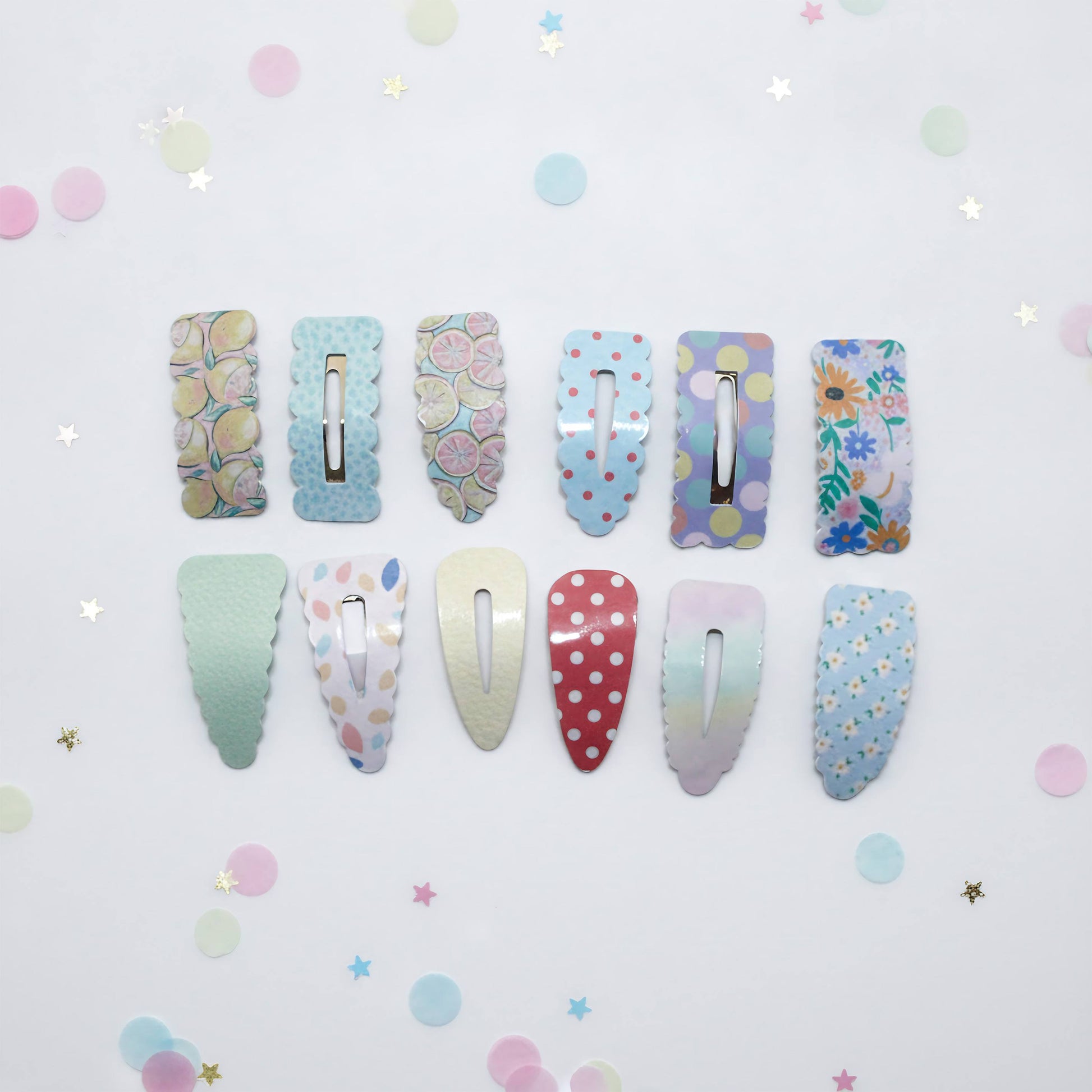 Twelve pastel hair clips arranged in two rows on a white background with scattered pastel confetti. The clips feature various patterns including polka dots, floral prints, and solid pastel colors.