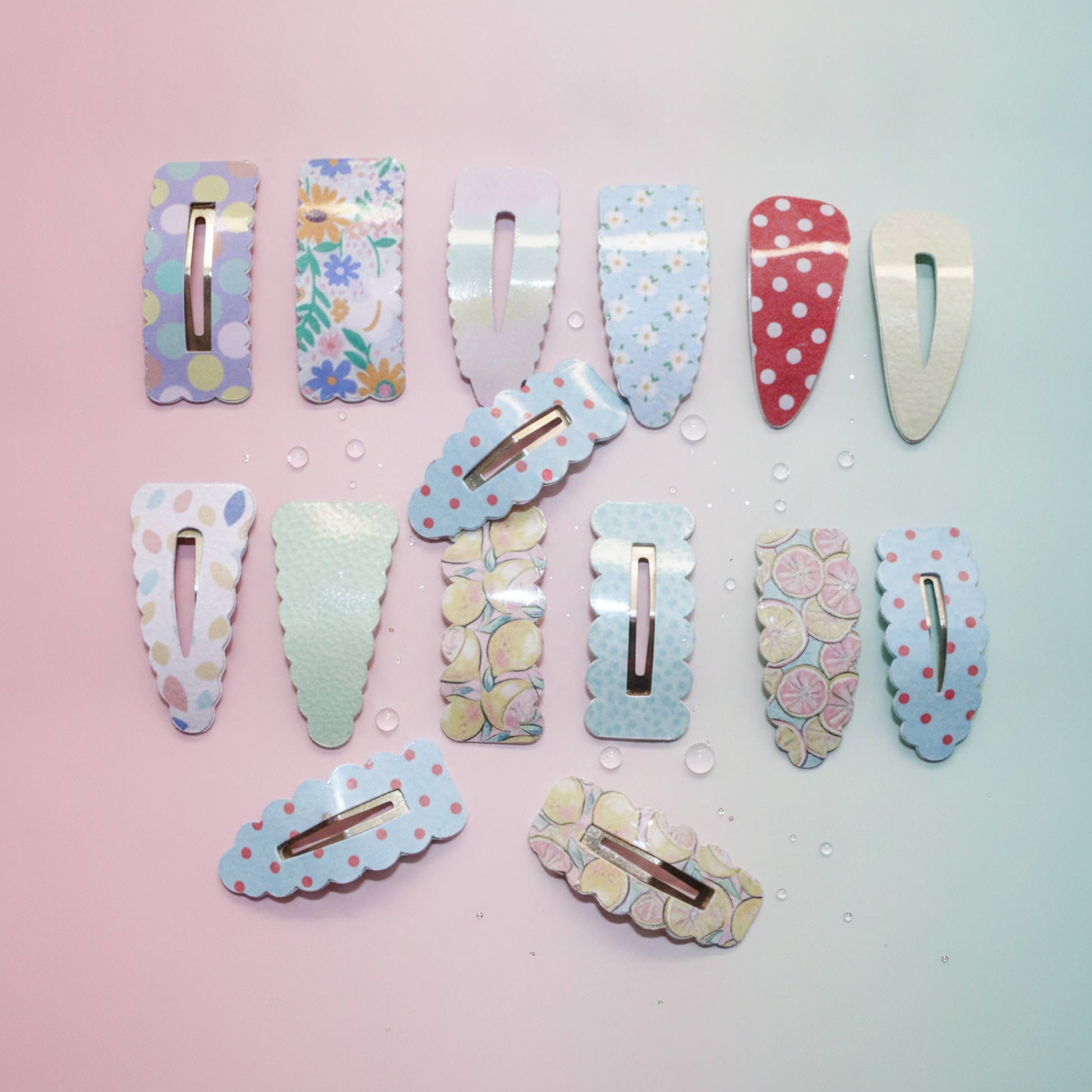 Twelve pastel hair claw clips with various patterns and designs, arranged on a pastel pink and blue gradient background with small water droplets.