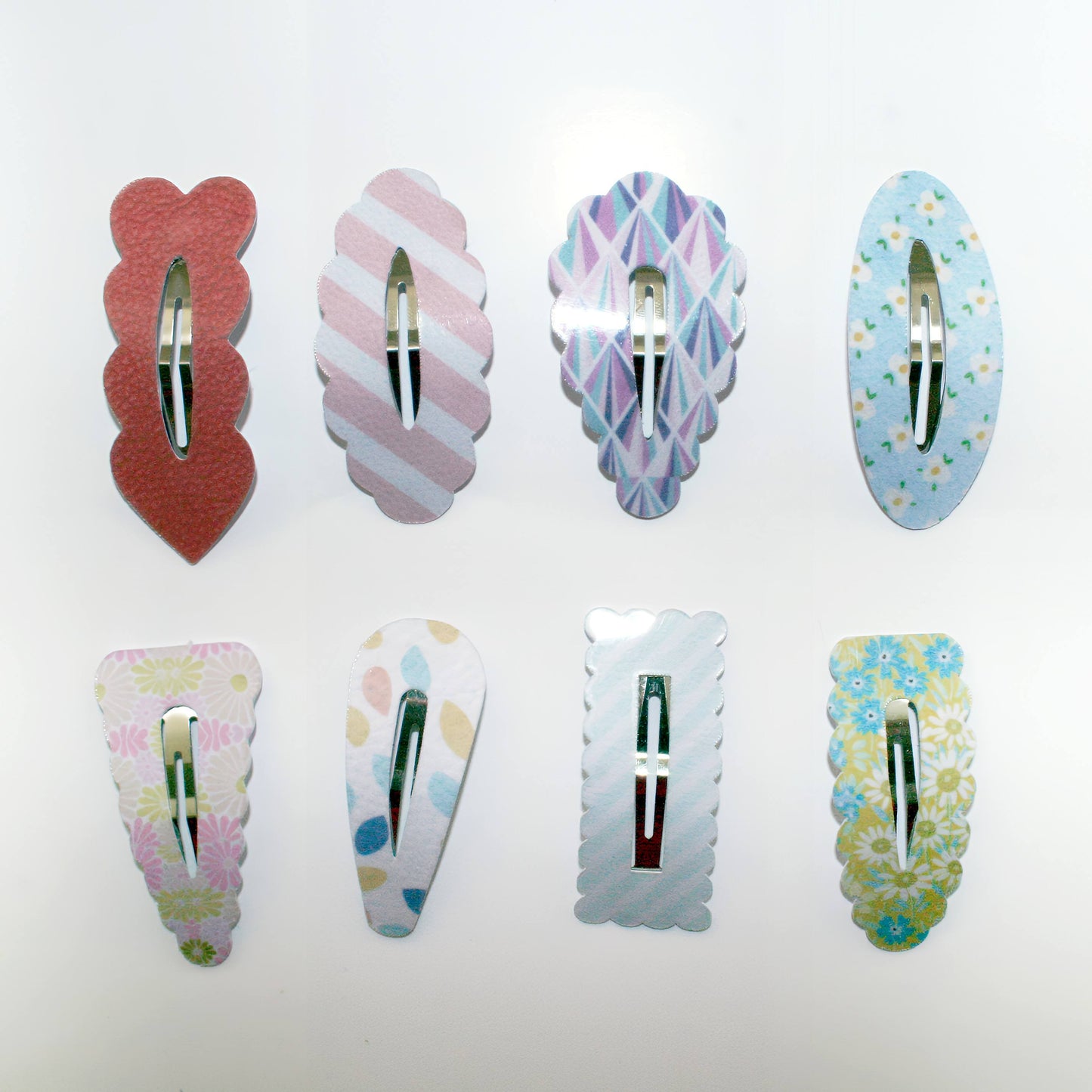 Six decorative hair claw clips arranged in two rows on a plain white background. The clips have scalloped edges and various pastel patterns including stripes, florals, and geometric designs, with silver metal clasps.