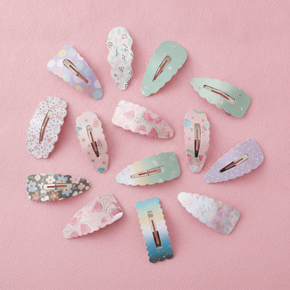 A set of pastel decorative hair clips arranged on a soft pink background. The clips feature various patterns including floral prints, polka dots, stars, and watercolor gradients in light blue, mint green, lavender, and pink, with rose gold metal clasps visible.