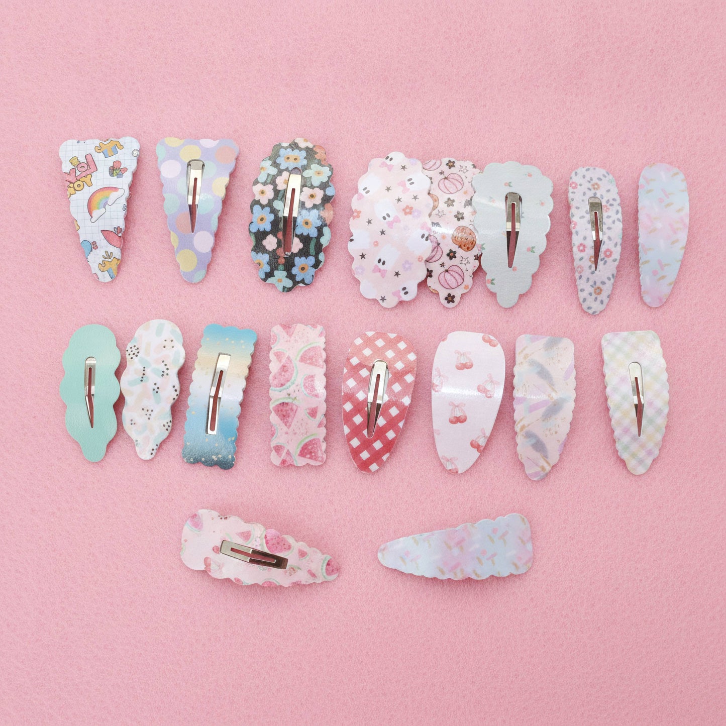 Twelve decorative hair claw clips arranged in rows on a solid pink background. The clips feature various pastel patterns including florals, checkers, stripes, and cute illustrations, with silver metal spring clips visible at the back.