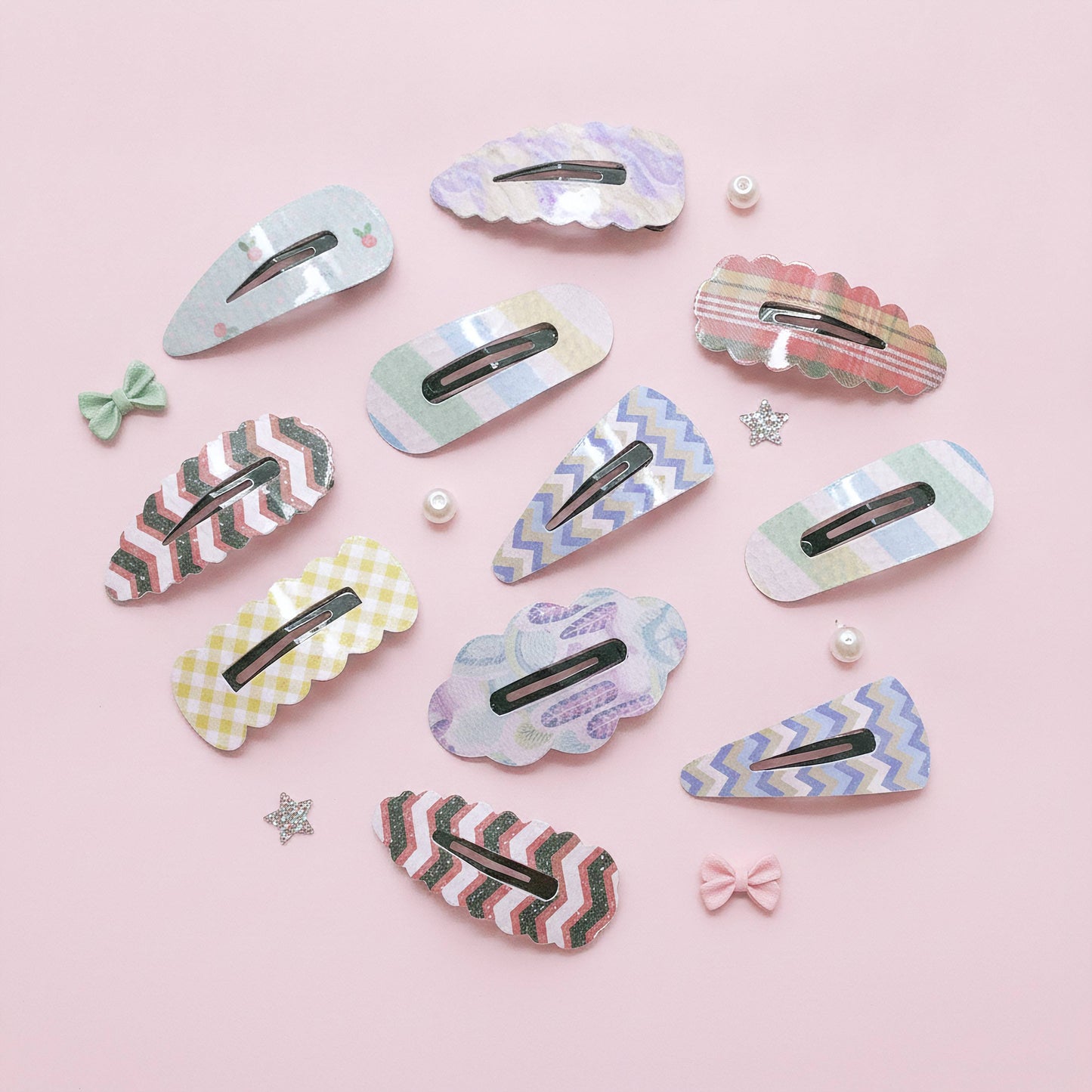 A set of pastel patterned hair clips arranged on a light pink background with small decorative bows, pearls, and star stickers.