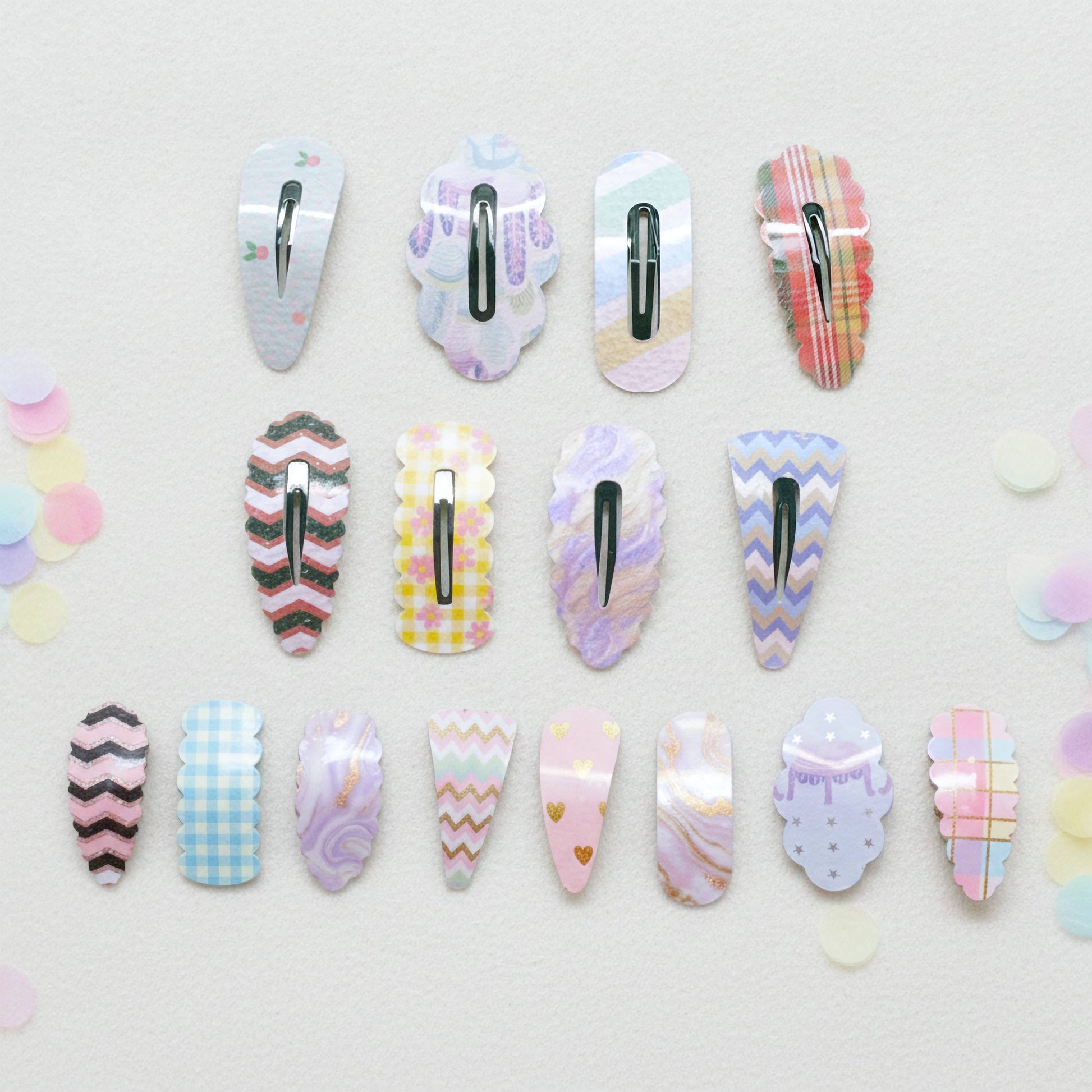 Twelve decorative hair claw clips arranged in three rows on a light textured background with pastel confetti. The clips feature various pastel patterns including plaid, chevron, gingham, marble, and polka dots in pink, purple, blue, yellow, and white.