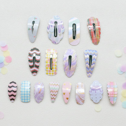 Twelve decorative hair claw clips arranged in three rows on a light textured background with pastel confetti. The clips feature various pastel patterns including plaid, chevron, gingham, marble, and polka dots in pink, purple, blue, yellow, and white.