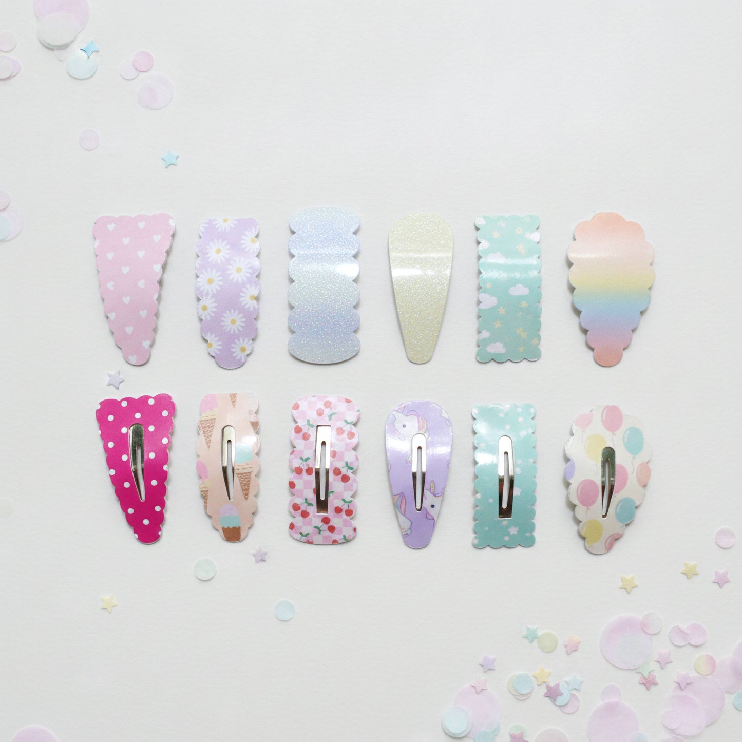 Twelve pastel hair claw clips arranged in two rows on a white background with scattered pastel confetti. The clips feature various patterns including polka dots, daisies, florals, and a rainbow gradient.