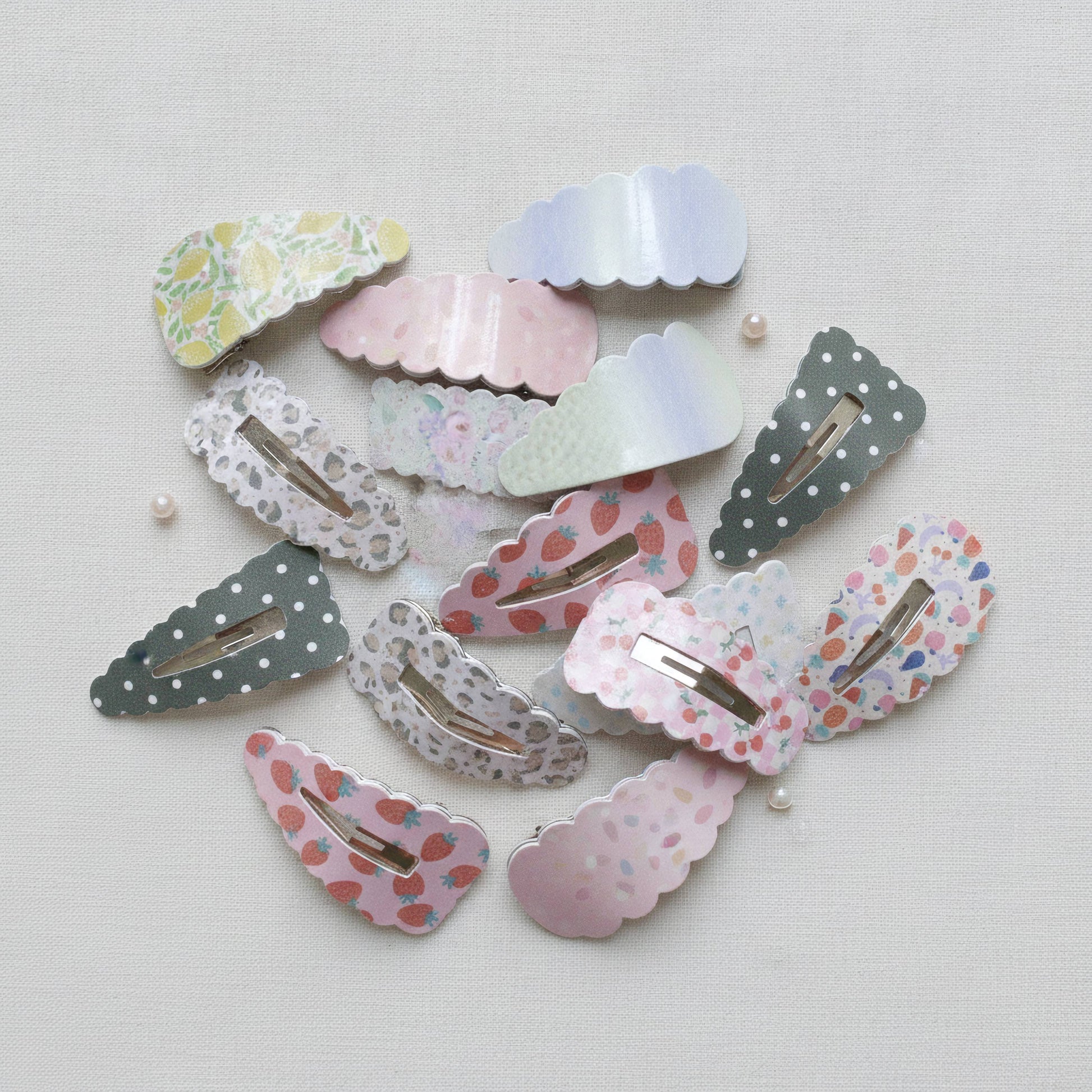 A collection of pastel-colored hair claw clips with various patterns including polka dots, floral prints, lace, and strawberry motifs, arranged on a light textured fabric background.