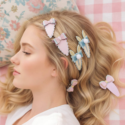 A woman with long wavy blonde hair wearing six pastel hair clips, posed against a pink and white checkered pillow and a floral pillow.