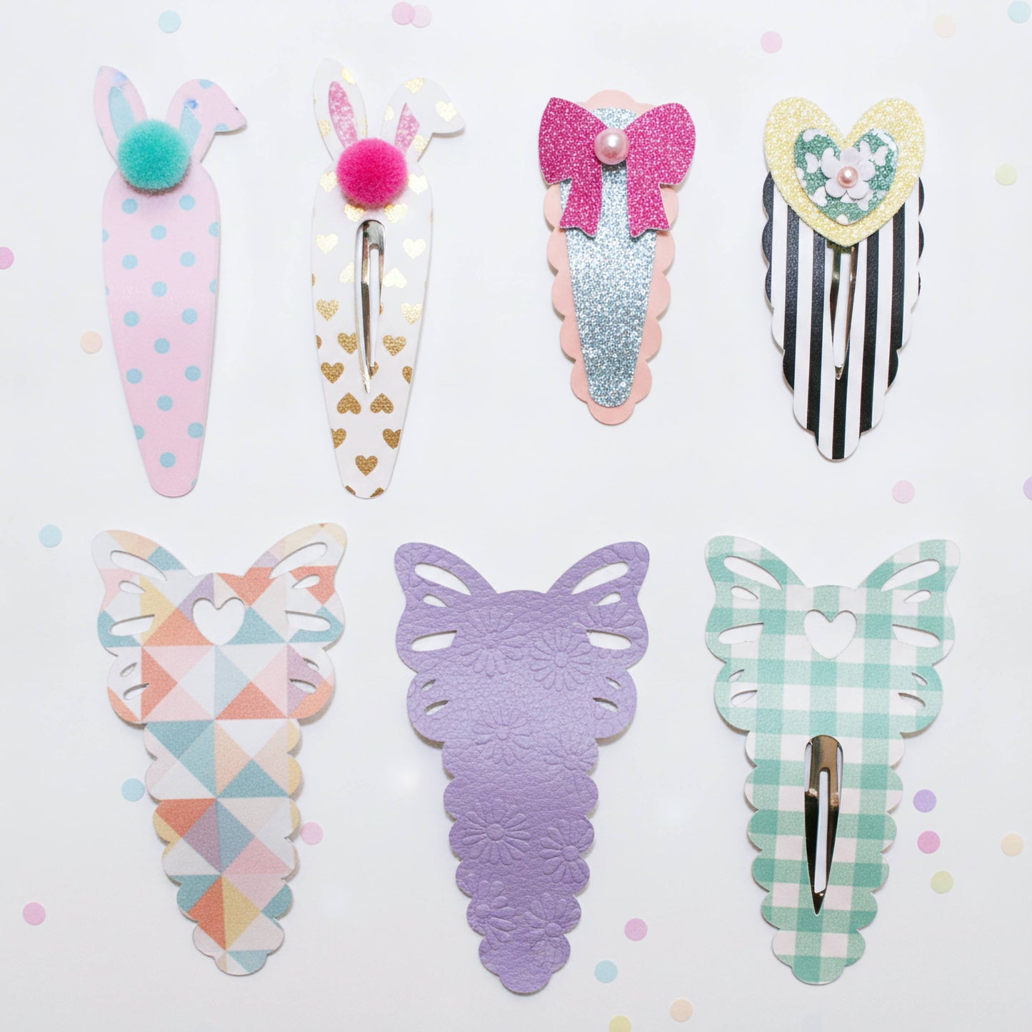 A set of eight pastel hair clips arranged on a light pink background. The clips feature bunny, carrot, bow, heart, and butterfly designs in soft pastel colors including pink, lavender, mint green, white, and glittery rose gold.