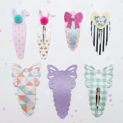 A set of eight pastel hair clips arranged on a light pink background. The clips feature bunny, carrot, bow, heart, and butterfly designs in soft pastel colors including pink, lavender, mint green, white, and glittery rose gold.