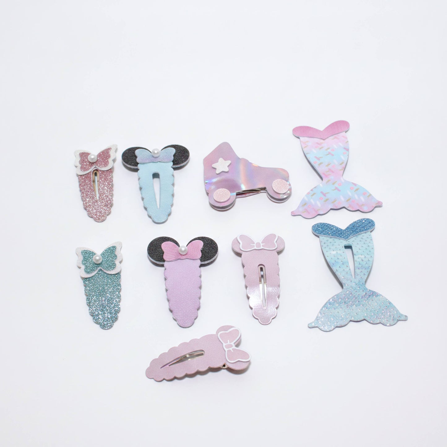A set of eight pastel mermaid-themed hair clips arranged on a plain white background. The clips feature various designs including glittery mermaid tails, bows, Minnie Mouse-style ears, and an iridescent roller skate with a star.