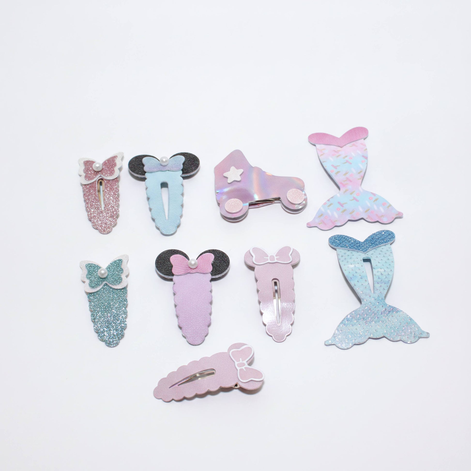 A set of eight pastel mermaid-themed hair clips arranged on a plain white background. The clips feature various designs including glittery mermaid tails, bows, Minnie Mouse-style ears, and an iridescent roller skate with a star.