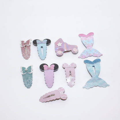 A set of eight pastel mermaid-themed hair clips arranged on a plain white background. The clips feature various designs including glittery mermaid tails, bows, Minnie Mouse-style ears, and an iridescent roller skate with a star.