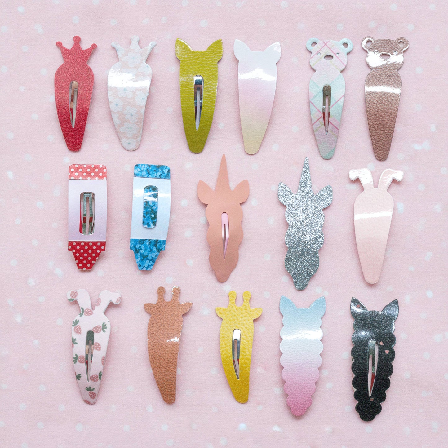 A set of 15 cute animal-shaped hair clips arranged in a grid on a light pink background with white dots. The clips feature various pastel and metallic colors, including red, white, green, pink, silver, yellow, and black, with designs resembling a carrot, bunny, cat, giraffe, and bear.