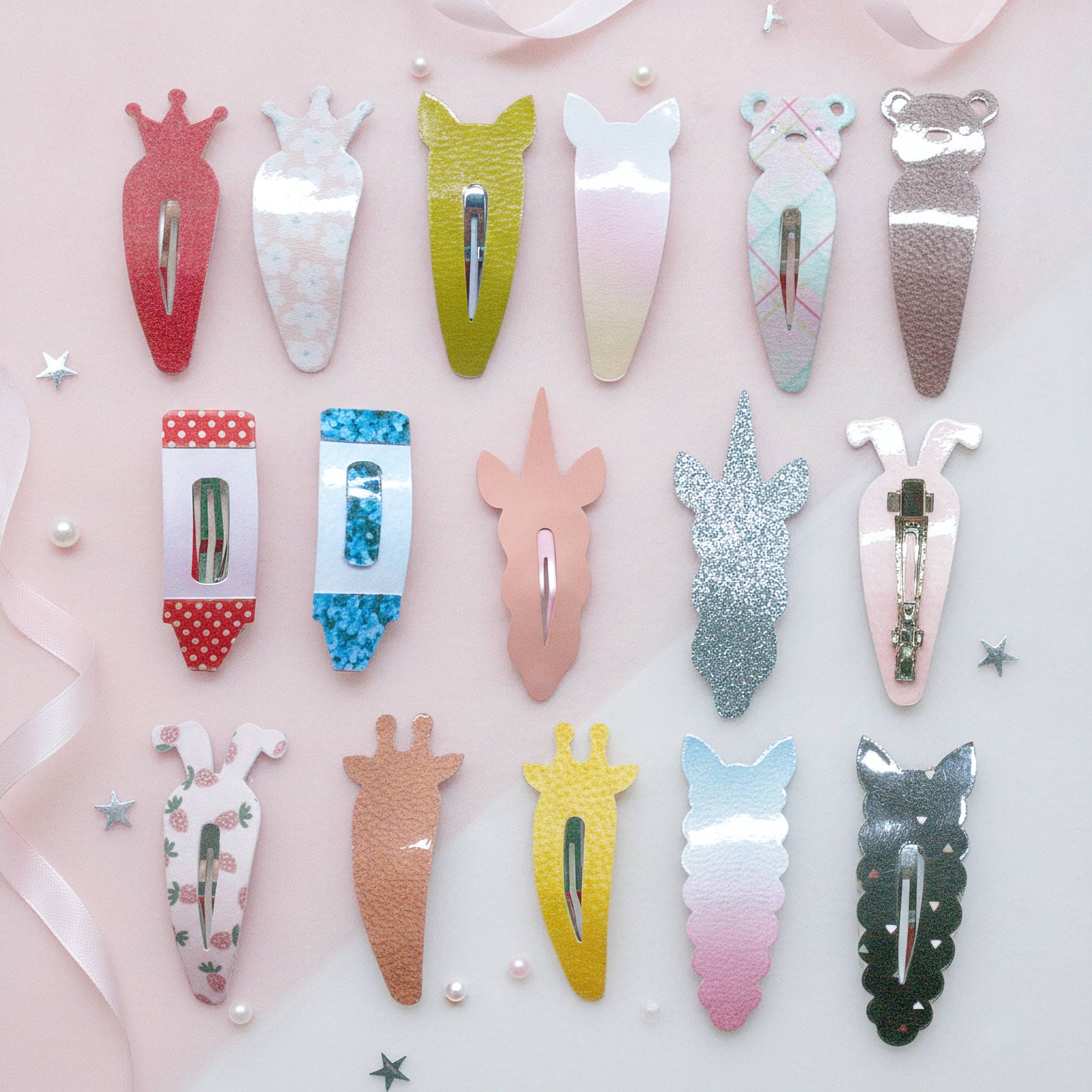 A set of 15 cute animal and vegetable-shaped hair clips arranged in rows on a light pink background with decorative ribbons and stars. The clips feature various designs including a carrot, a unicorn head, a bear, a cat, and different glitter and pastel finishes.