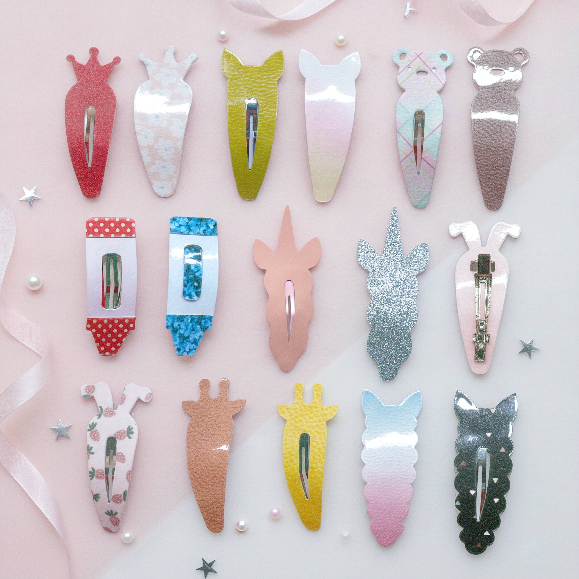 A set of 15 cute animal and vegetable-shaped hair clips arranged in rows on a light pink background with decorative ribbons and stars. The clips feature various designs including a carrot, a unicorn head, a bear, a cat, and different glitter and pastel finishes.