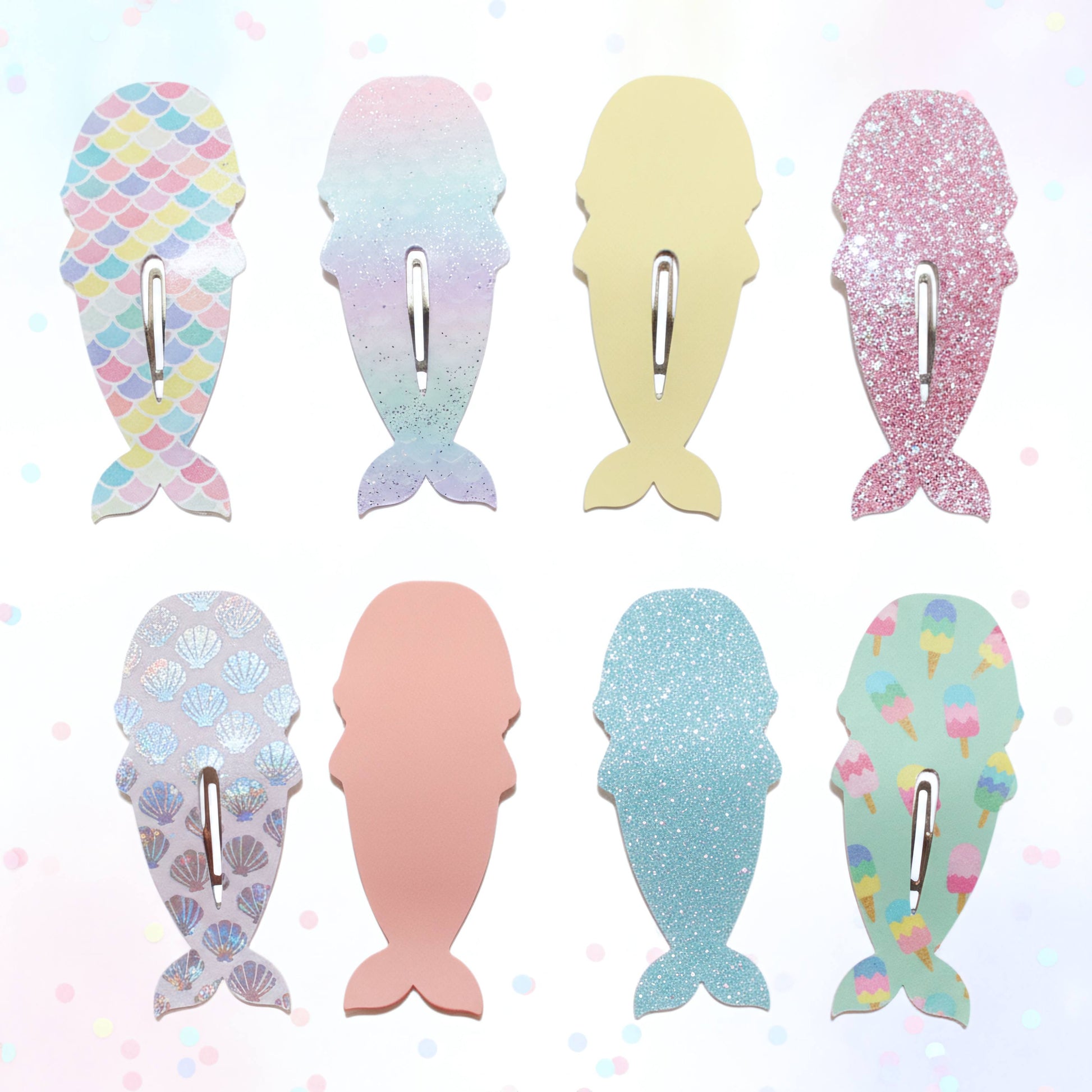 Eight mermaid tail-shaped hair clips arranged in a 2x4 grid on a light pastel background. The clips feature different designs: scales, iridescent gradient, solid pale yellow, glitter pink, scallop pattern, solid pale pink, glitter light blue, and ice cream print.