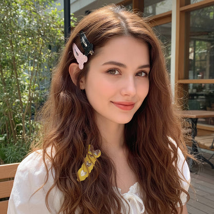 A woman with long, wavy light brown hair wearing a black and pink butterfly hair clip and a yellow floral hair tie, photographed outdoors in front of a cafe.