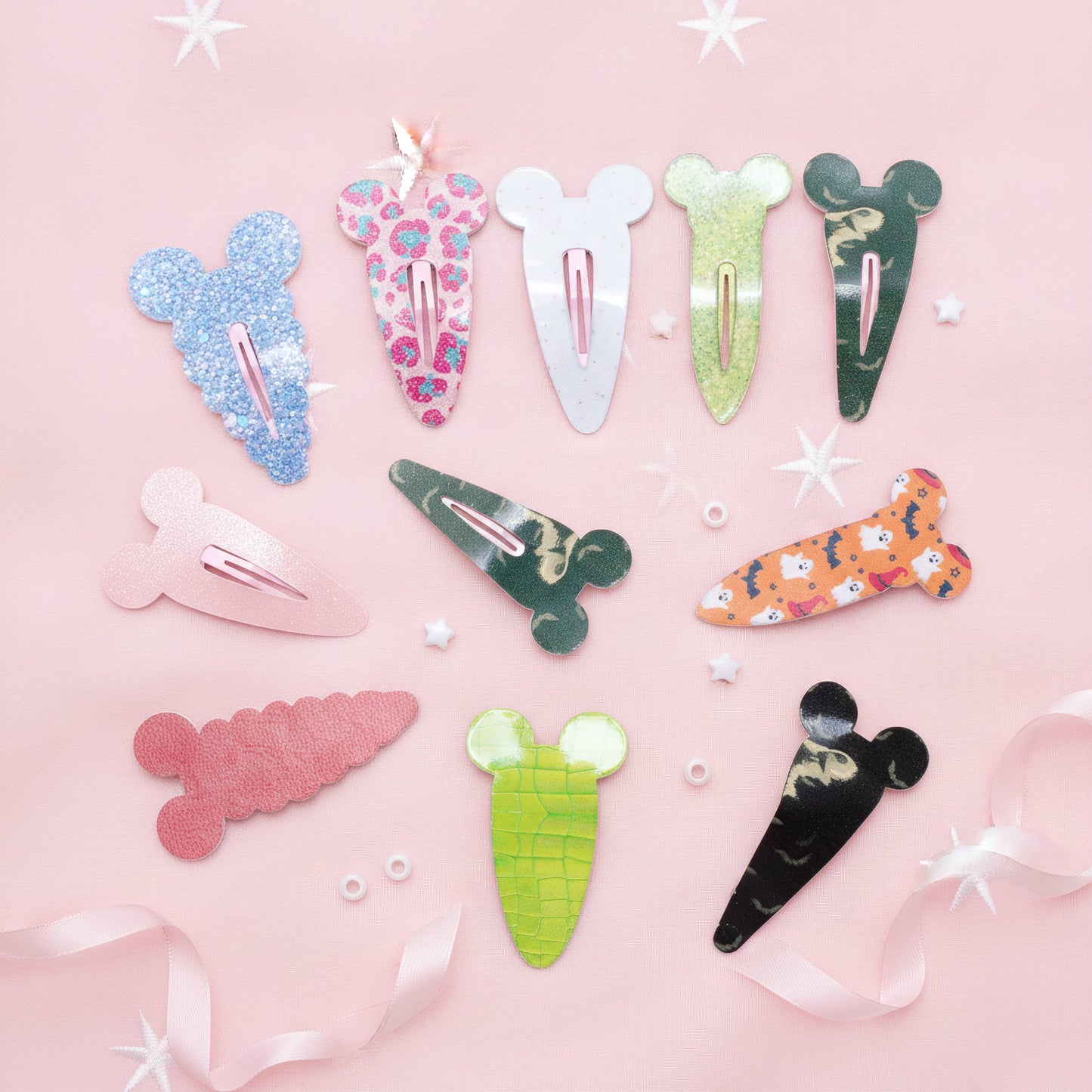 A flat-lay of nine colorful hair clips shaped like cartoon characters and vegetables, arranged on a light pink background with white star stickers and pink ribbon accents.
