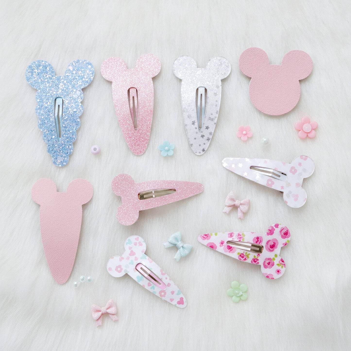 A set of pastel pink, blue, and white hair clips arranged on a white faux fur background. The set includes various shapes like Mouse ears, bows, and floral patterns.