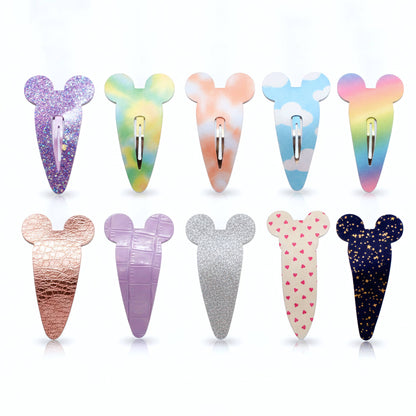Eight  Mouse-shaped hair clips in various designs and colors, arranged in two rows of four on a white background. The clips feature different patterns including glitter, tie-dye, rainbow, textured metallic, crocodile-embossed, silver glitter, pink hearts, and a dark blue starry night design.
