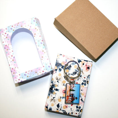 Floral keychain with a small tag on a white surface next to a cardboard box.