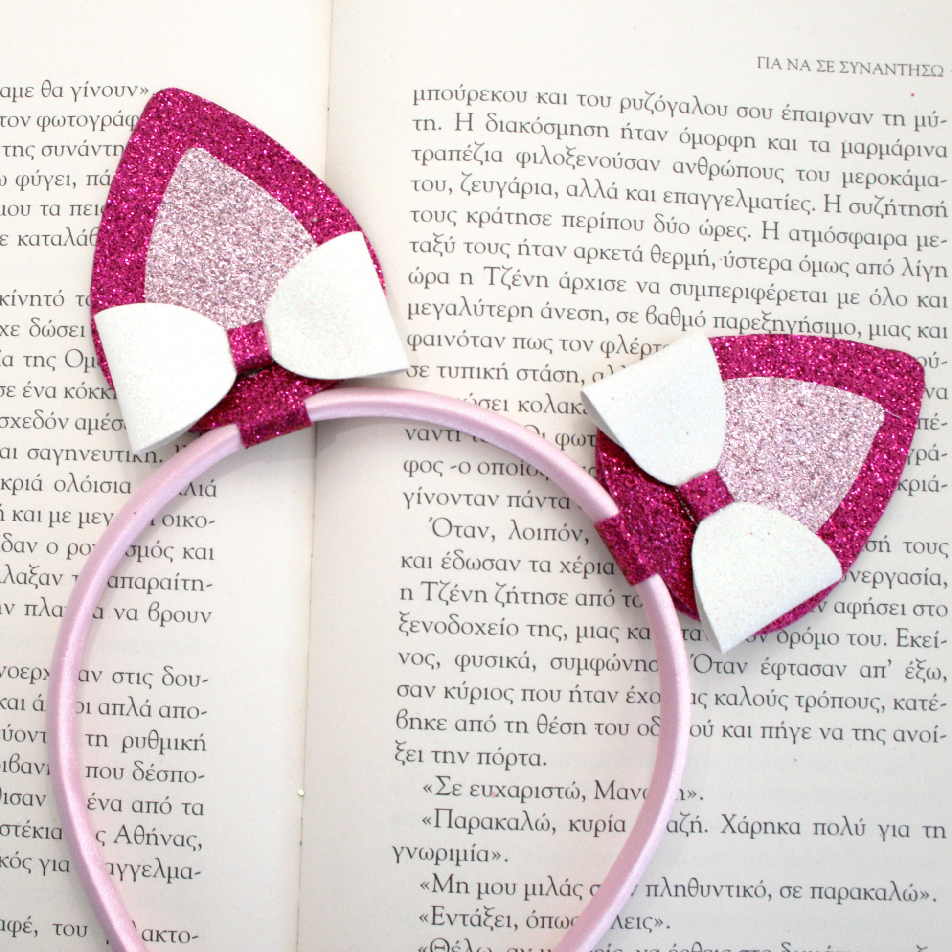 Photograph of a pink headband with glittery pink and white cat ears and a pink glittery butterfly clip, featuring a small pink plush bunny.