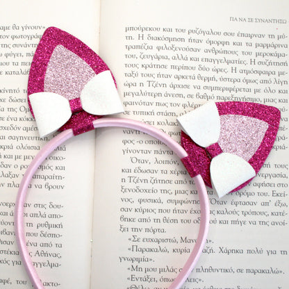 Photograph of a pink headband with glittery pink and white cat ears and a pink glittery butterfly clip, featuring a small pink plush bunny.