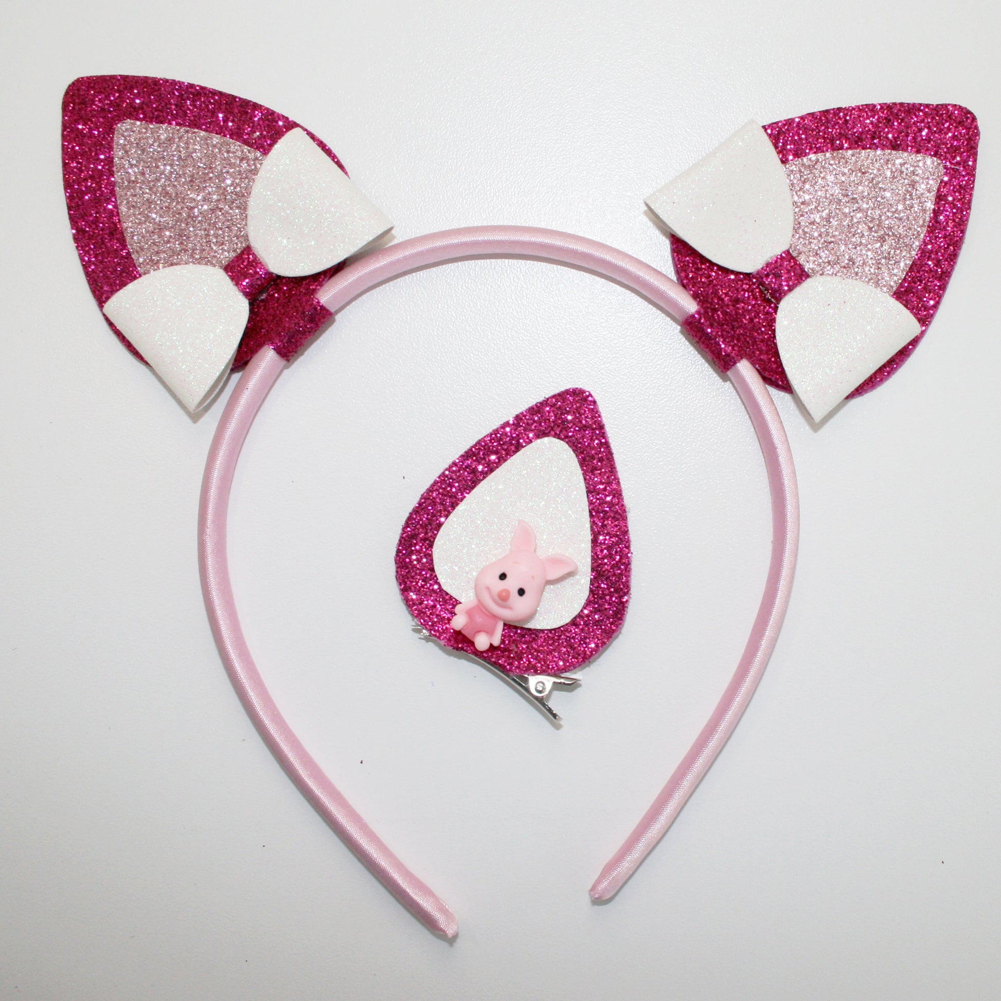 Photograph of a pink headband with glittery pink and white cat ears and a pink glittery butterfly clip, featuring a small pink plush bunny.