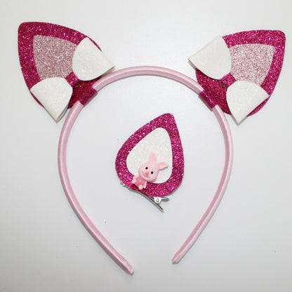 Photograph of a pink headband with glittery pink and white cat ears and a pink glittery butterfly clip, featuring a small pink plush bunny.