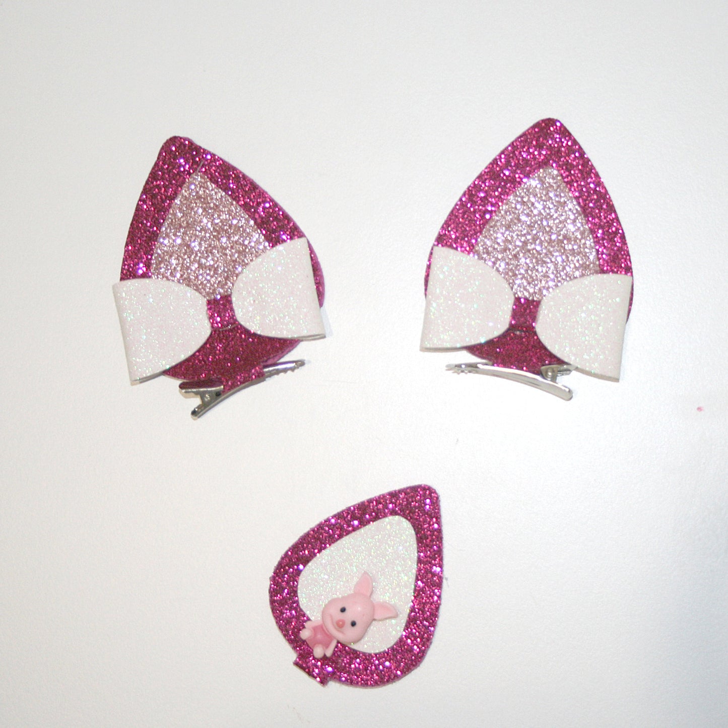  A close-up photograph of a pair of glittery, pink and white cat ear headbands with a small pink plush toy inside one ear. The background is plain white.