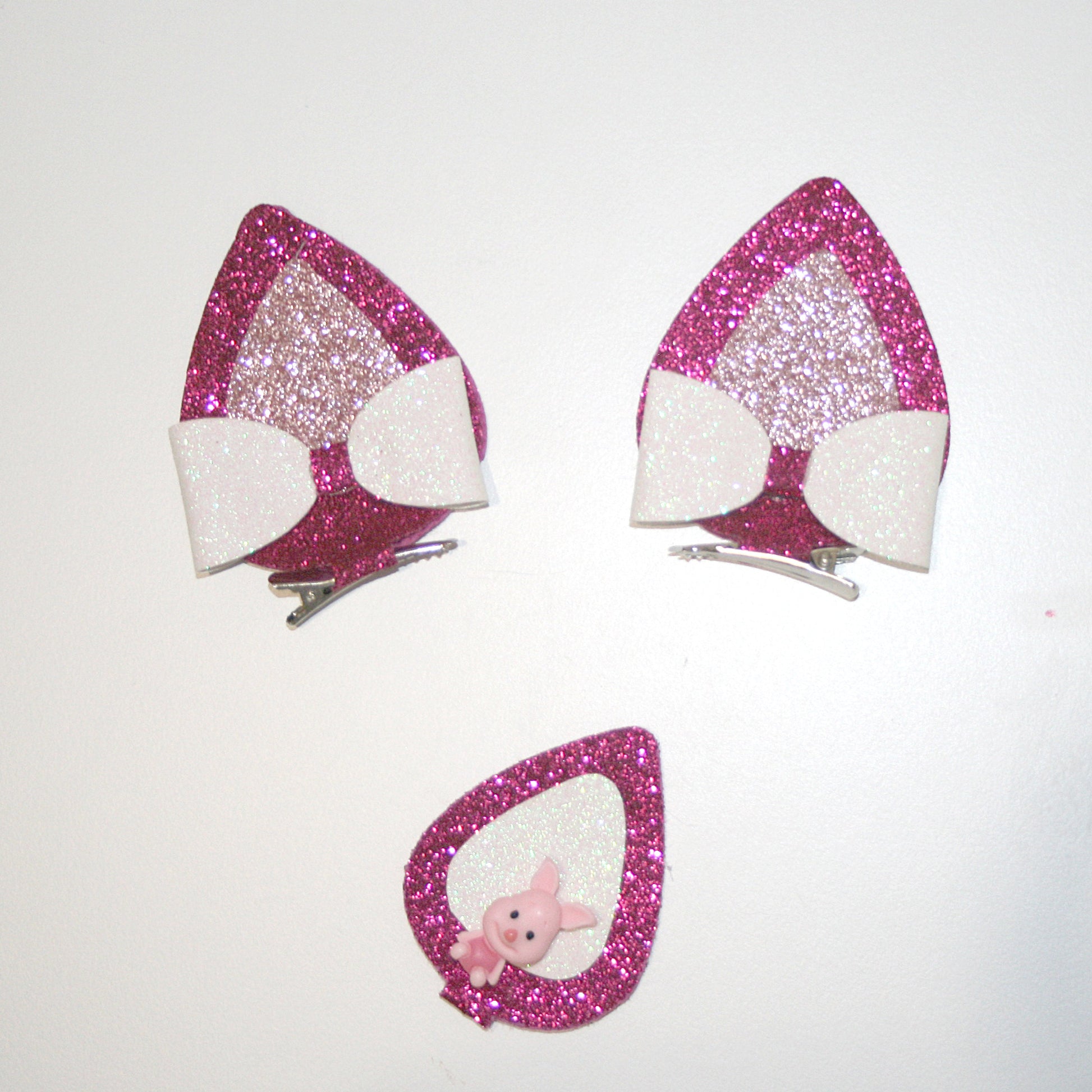  A close-up photograph of a pair of glittery, pink and white cat ear headbands with a small pink plush toy inside one ear. The background is plain white.